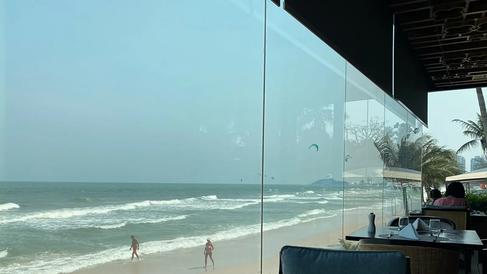 레스토랑-유리창밖으로-파도치는-후아힌해변에-두-명이-걷고-있다.